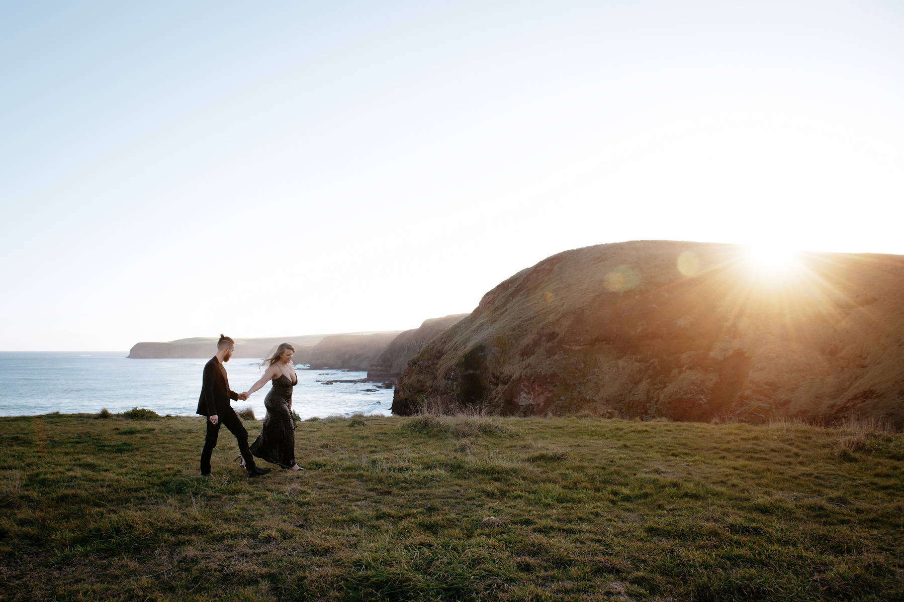 couple holding hands with woman in front on a hill with sunset