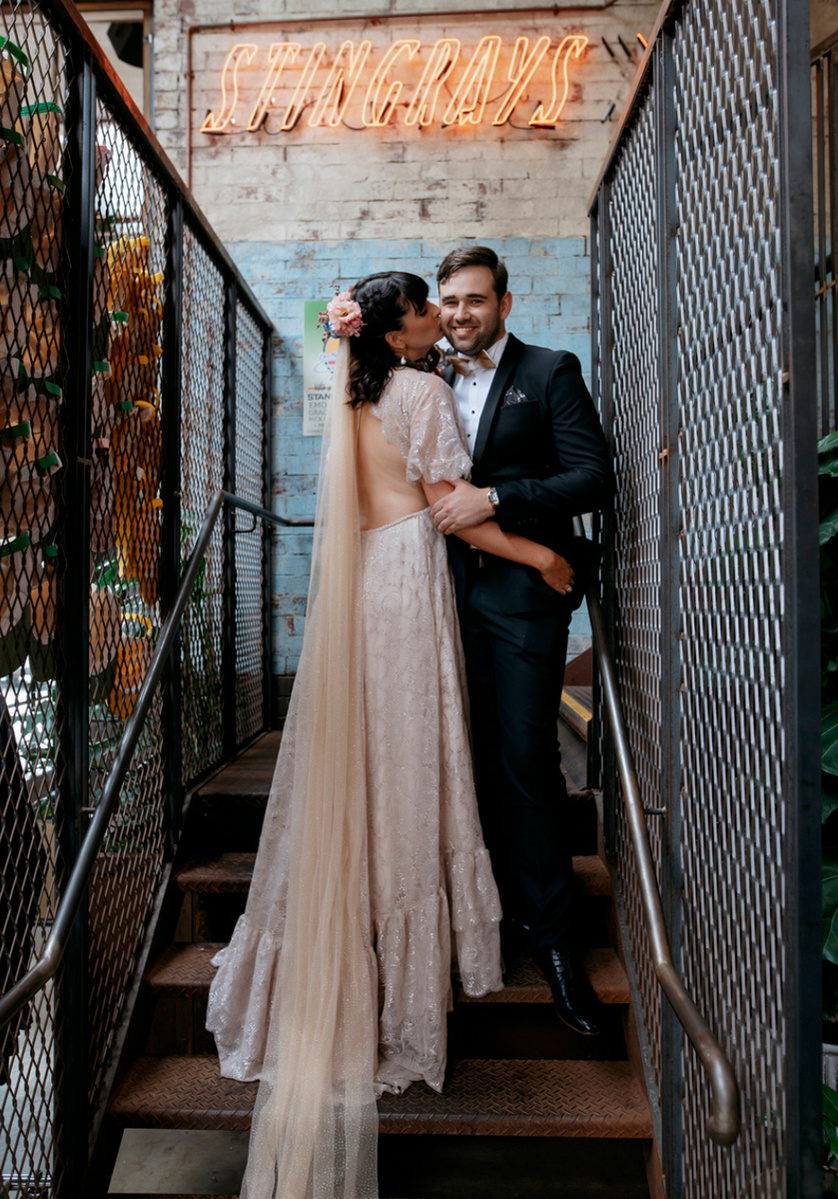 man in suite and woman in dress standing on stairs woman is kissing the mans cheek