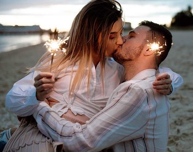 male and female kissing on beach holding sparklers