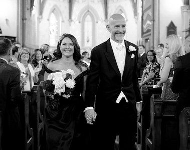 Bride and groom walking down church aisle smiling hand in hand. Black and white image. 