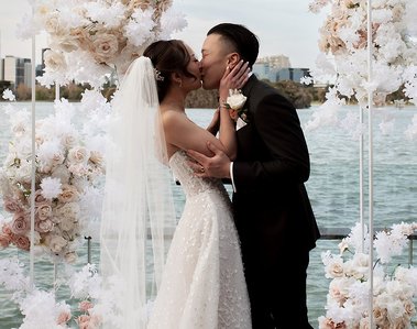 Bride and Groom kissing with flower display behind them and a lake. 