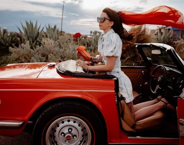 Woman in red car looking back her hair is blowing in the wind. woman holding red rose