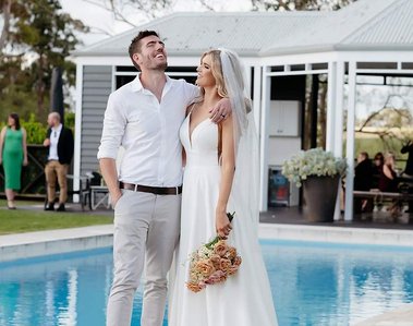 Groom with his arm around brides shoulder laughing in front of a pool. 