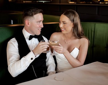 Bride and groom with cocktail glasses cheering looking at each other in booth sitting down