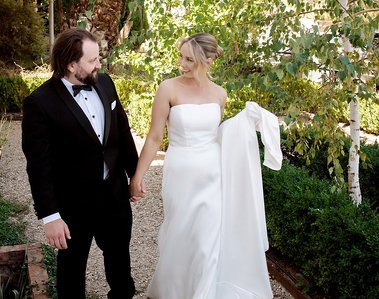 Bride and groom walking hand in hand looking at each other in a park greenery setting. 
