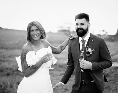 Black and white image of bride leaning her hand on grooms shoulder both holding Champagne glasses. 