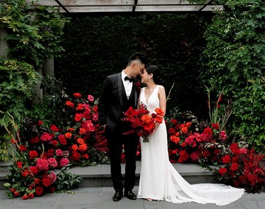 Bride and groom looking at each other in front of a red and pink curved floral display