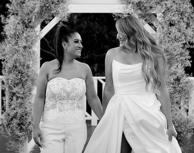 Two females in wedding dresses looking into each others eyes with altar behind them. black and white photo.