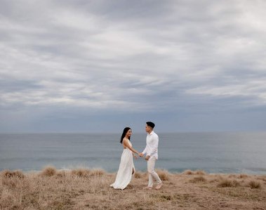 male and female holding hands on edge of cliff with view of the ocean