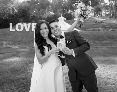 black and white image of bride and groom. Both holding Champagne glasses looking towards the camera, bride holding her bouquet high in the air. 