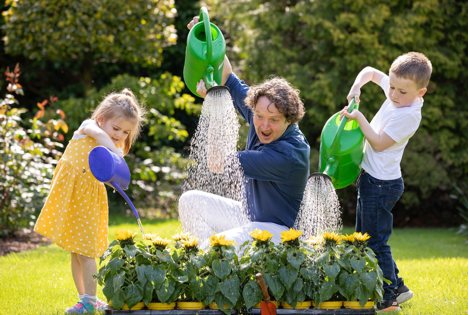 Irish garden designer and television personality Diarmuid Gavin pouring water from a watering can with two children at a Press PR Photocall for Irish Hospice Sunflower Appeal