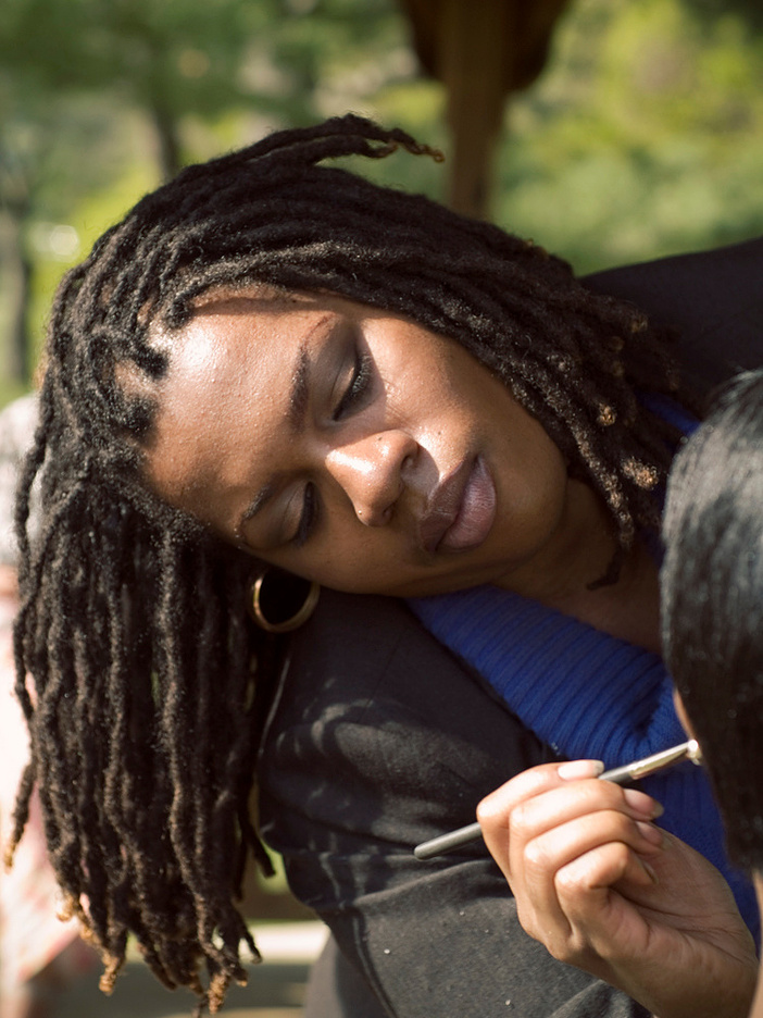 Kenya Morris does makeup outdoors in a beautiful setting. Kenya is focused, yet not stressed at all. She embodies flow. This image was photographed by Vincent Hunter.