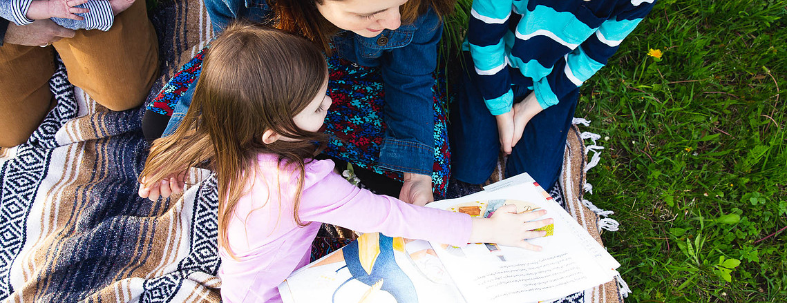 Mom and two kids on a blanket reading a book