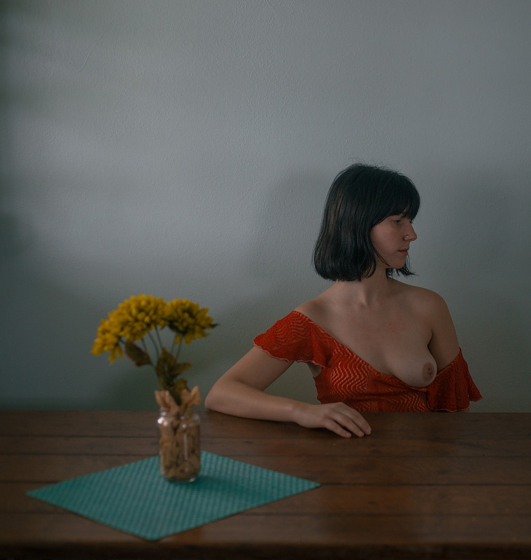 Girl sits at table wearing red dress, exposes breast