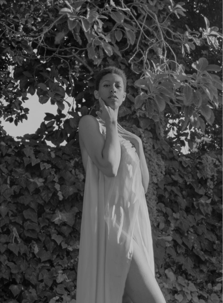 Black and white photo of woman standing gracefully wearing silk in front of tree