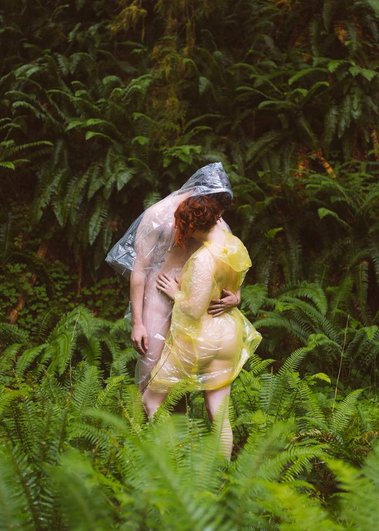 Couple embraces in rain ponchos surrounded by ferns in Hoh Rainforest, Olympic National Park, Washington