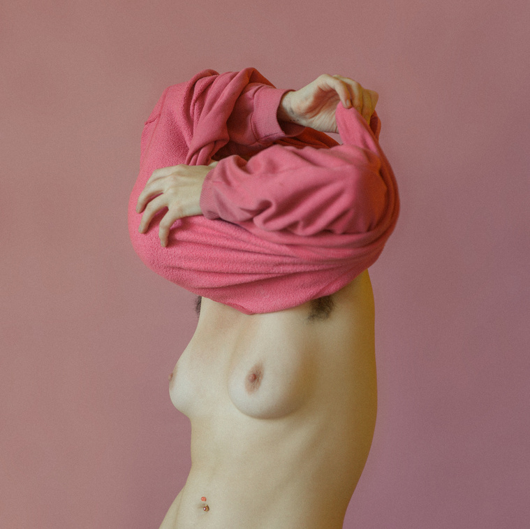 Nude woman struggles to remove pink sweater