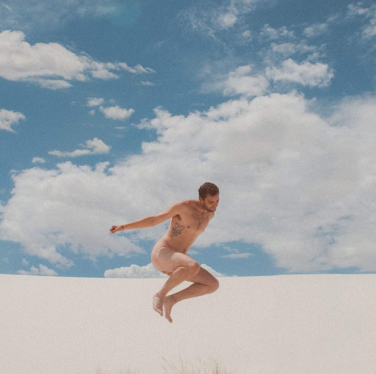 Film nude man jumping against blue cloudy sky in White Sands National Monument, New Mexico