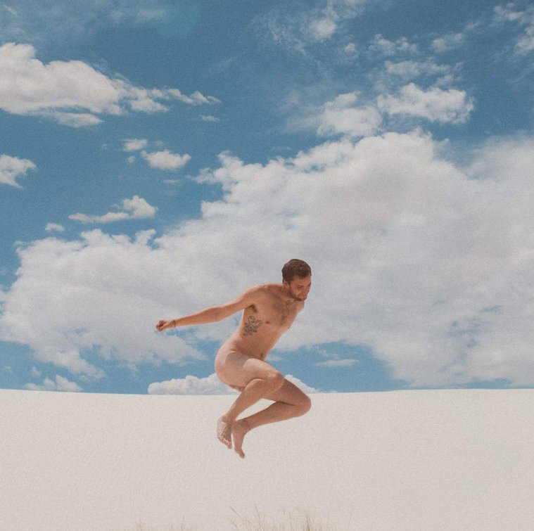 Film nude man jumping against blue cloudy sky in White Sands National Monument, New Mexico