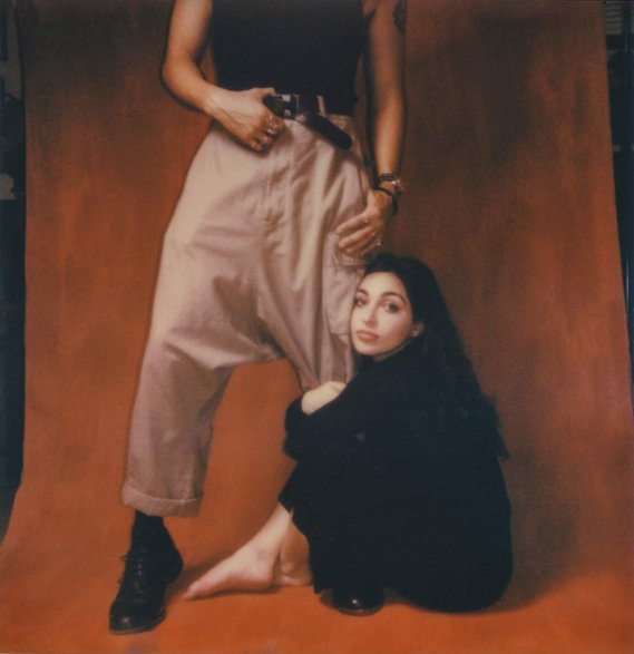Polaroid of woman holding mans leg against red backdrop
