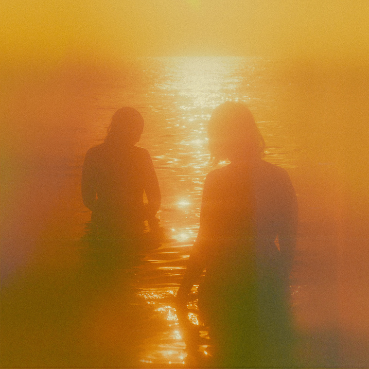Vintage film photo of two women silhouetted against orange and yellow ocean sunset