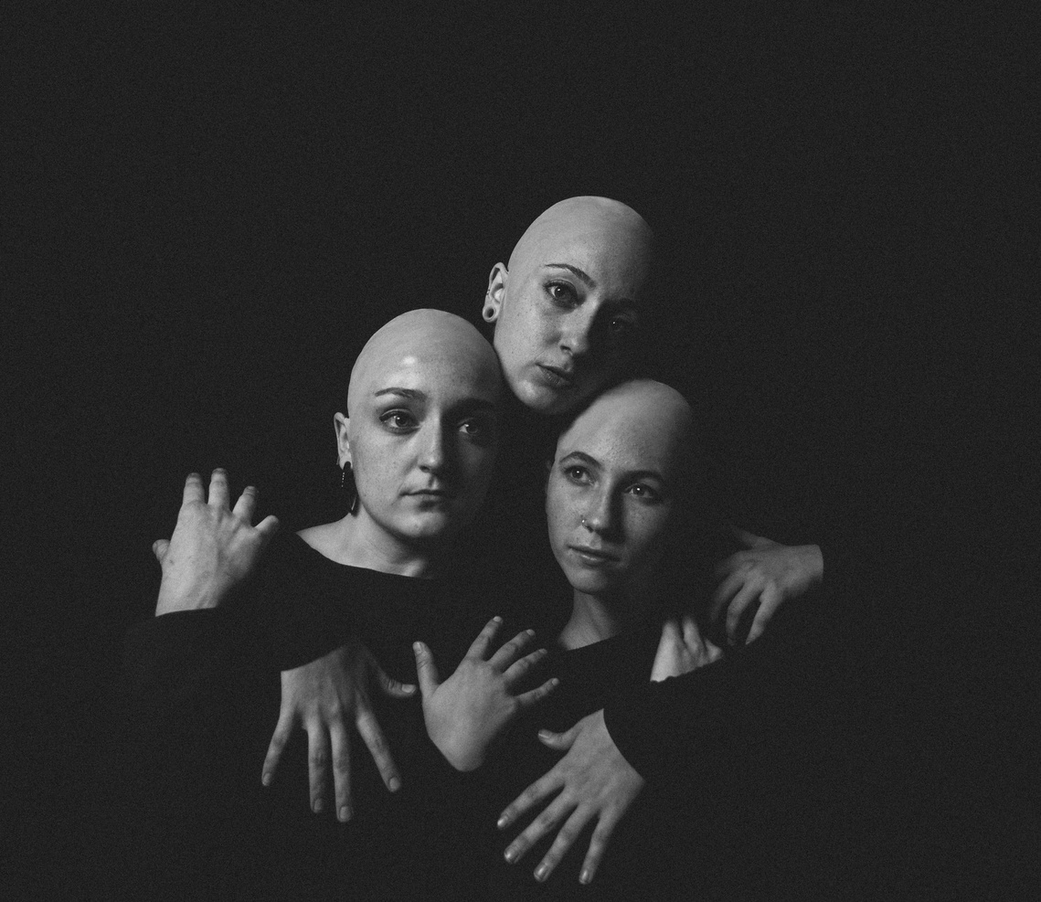 Black and white studio portrait of three bald sisters