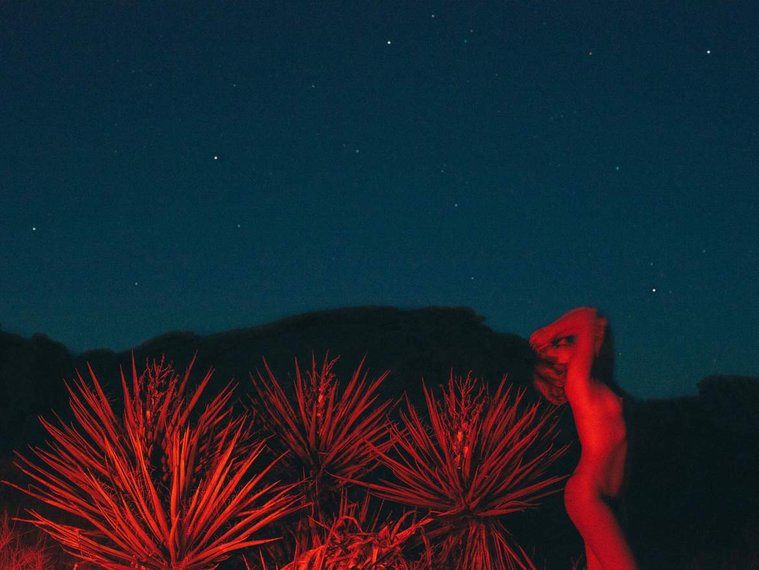 Red light nude at night with Yucca trees in Joshua Tree National Park, California, against blue starry sky
