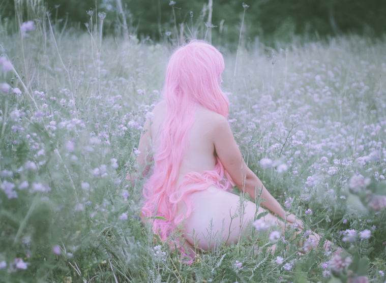 Nude woman with pink hair lounges in pastel flower field