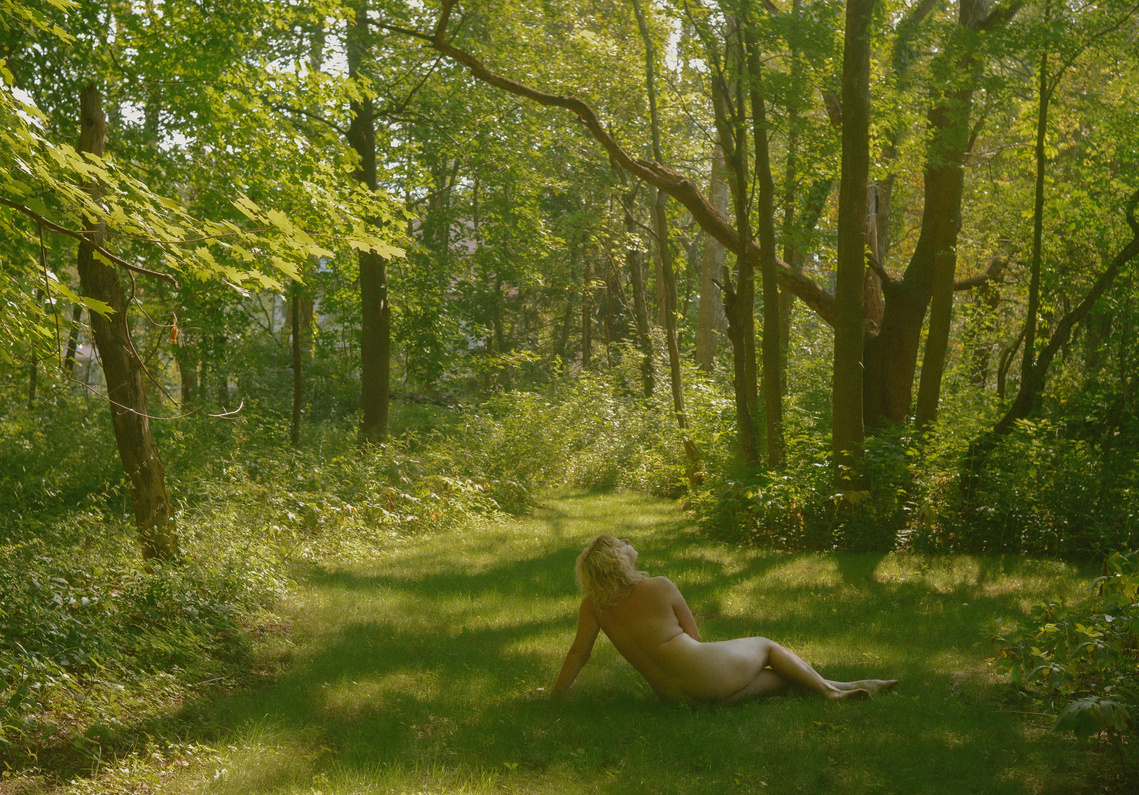 Nude woman lounges in lush green grass surrounded by trees