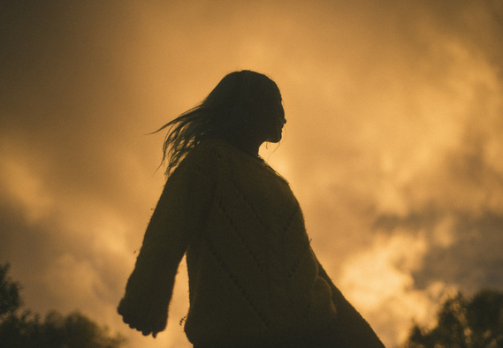 Silhouetted girl spins and flips hair in front of yellow clouds at sunset