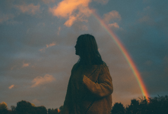 Vintage film photo, girl stands in front of rainbow and cloudy sky