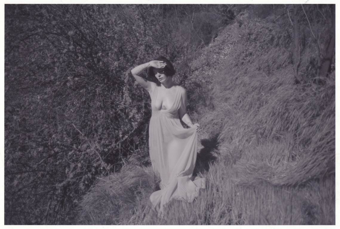 Black and white photo of woman standing on hillside in vintage dress