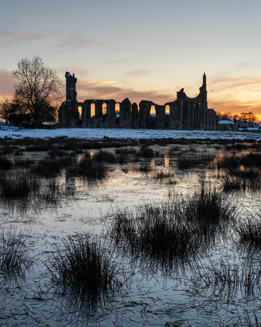 The sun sets behind a snowy Byland Abbey, North Yorkshire, UK. A photograph by Tim Pearson.