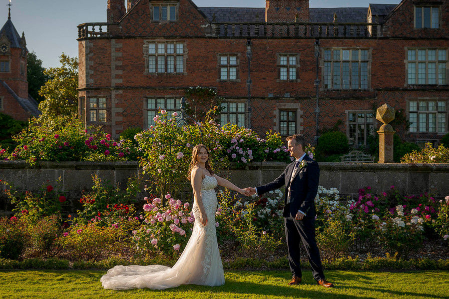 natural and authentic wedding photography, bride and groom holding hands at golden hour with stately home venue behind them