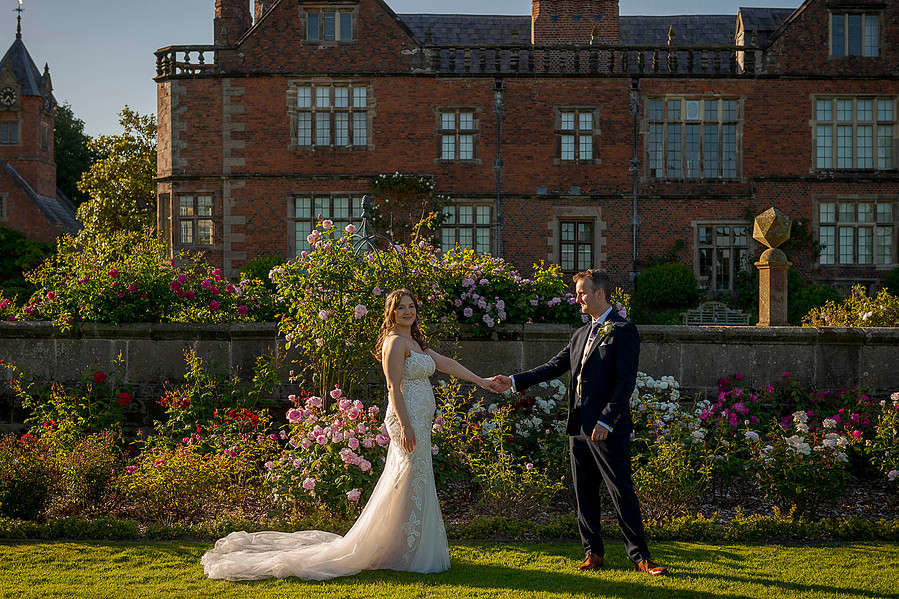 natural and authentic wedding photography, bride and groom holding hands at golden hour with stately home venue behind them