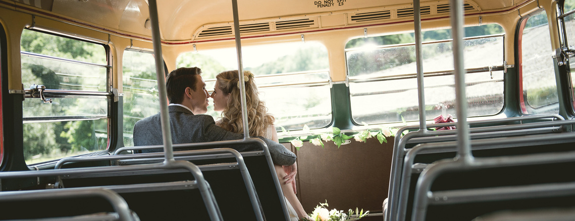 bride and groom sat on front seat of a double decker bus. bride holds bouquet of flowers