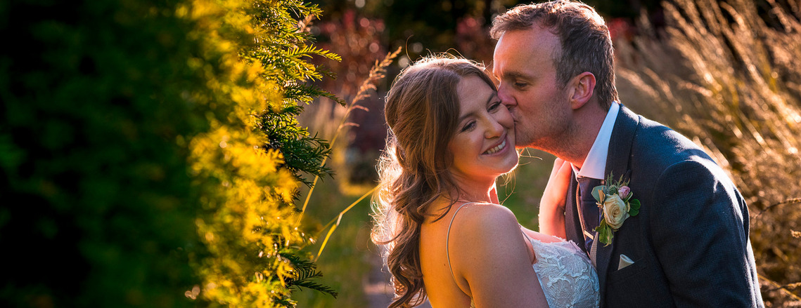 natural and relaxed wedding photography, candid shot of bride and groom cuddling in the gardens of venue