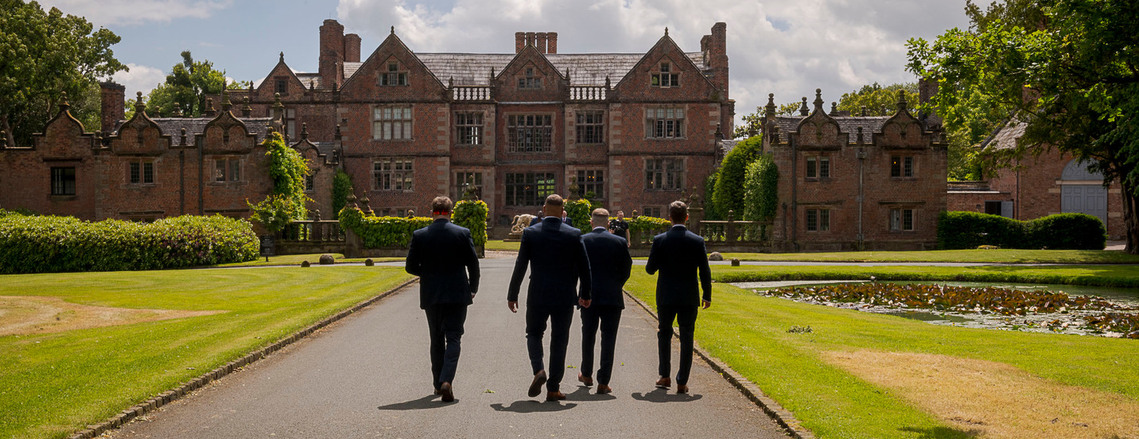 natural and relaxed wedding photography, candid shot of groom and groomsmen walking away from camera with stately home in background