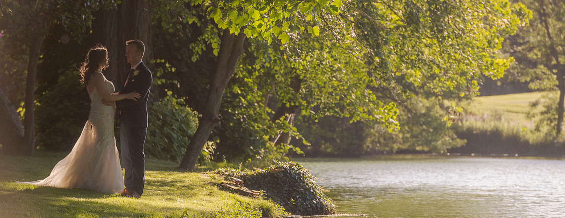 authentic wedding photography, bride and groom slow dance on the grass next to a lake at sunset