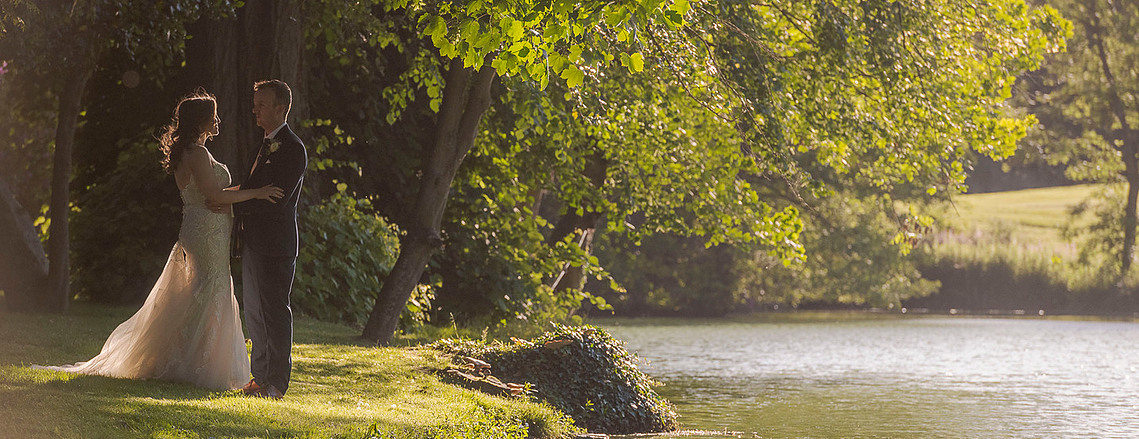 authentic wedding photography, bride and groom slow dance on the grass next to a lake at sunset