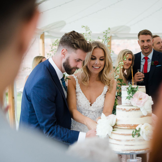 wedding photography, bride and groom cutting cake while guests look on
