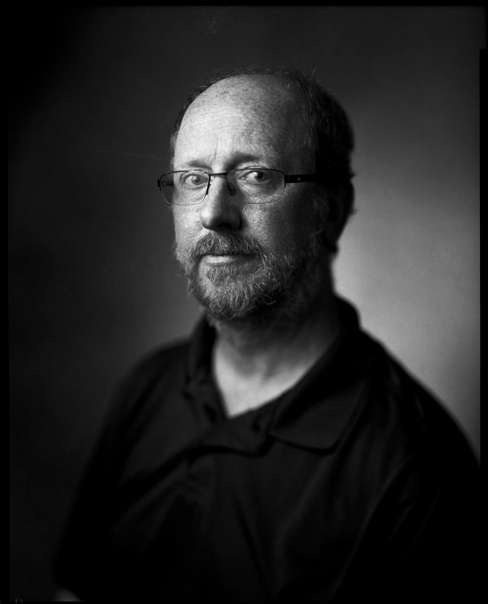 Large format paper negative self portrait of a man wearing glasses in studio setting.