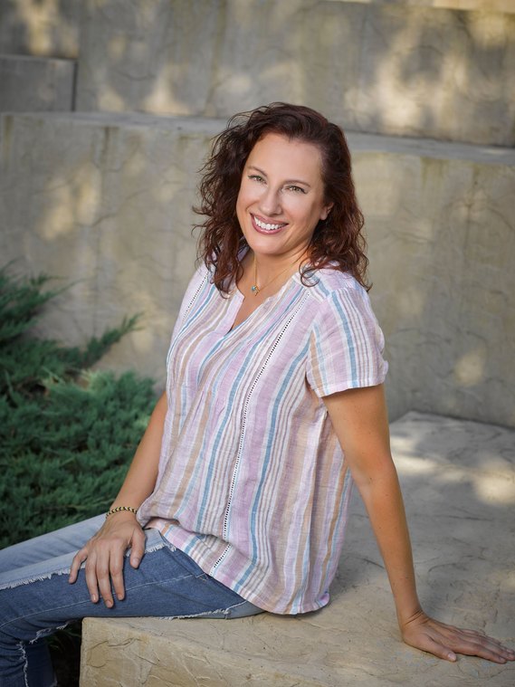 Outdoor branding image of Life coach sitting on large stone block with similar stone wall in background.