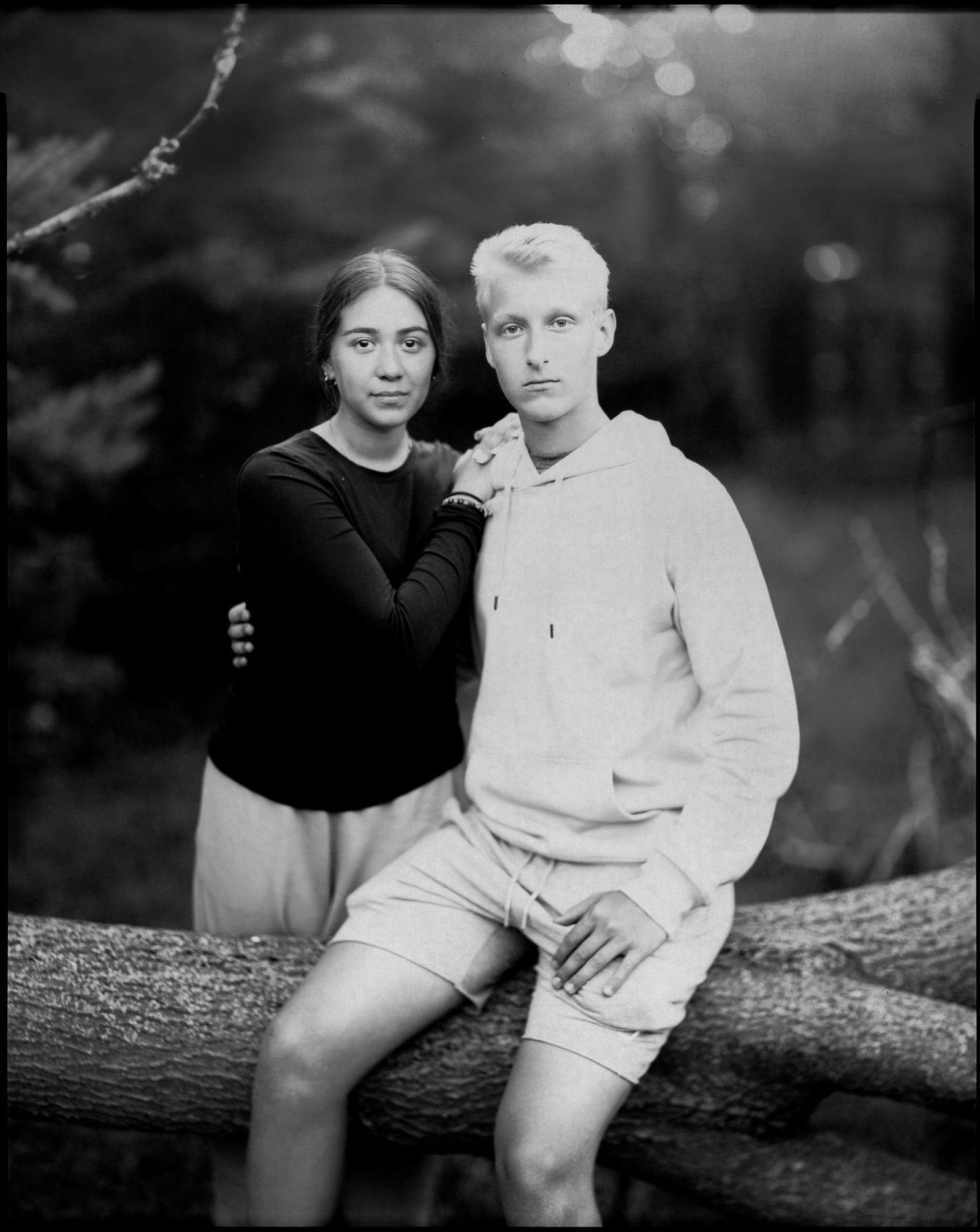 Large format paper negative portrait of a young man and woman outdoors sitting on fallen tree.