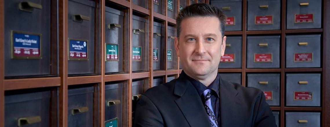An expressive Environmental Business portrait of an Executive leaning against a wall of loose tea drawers.