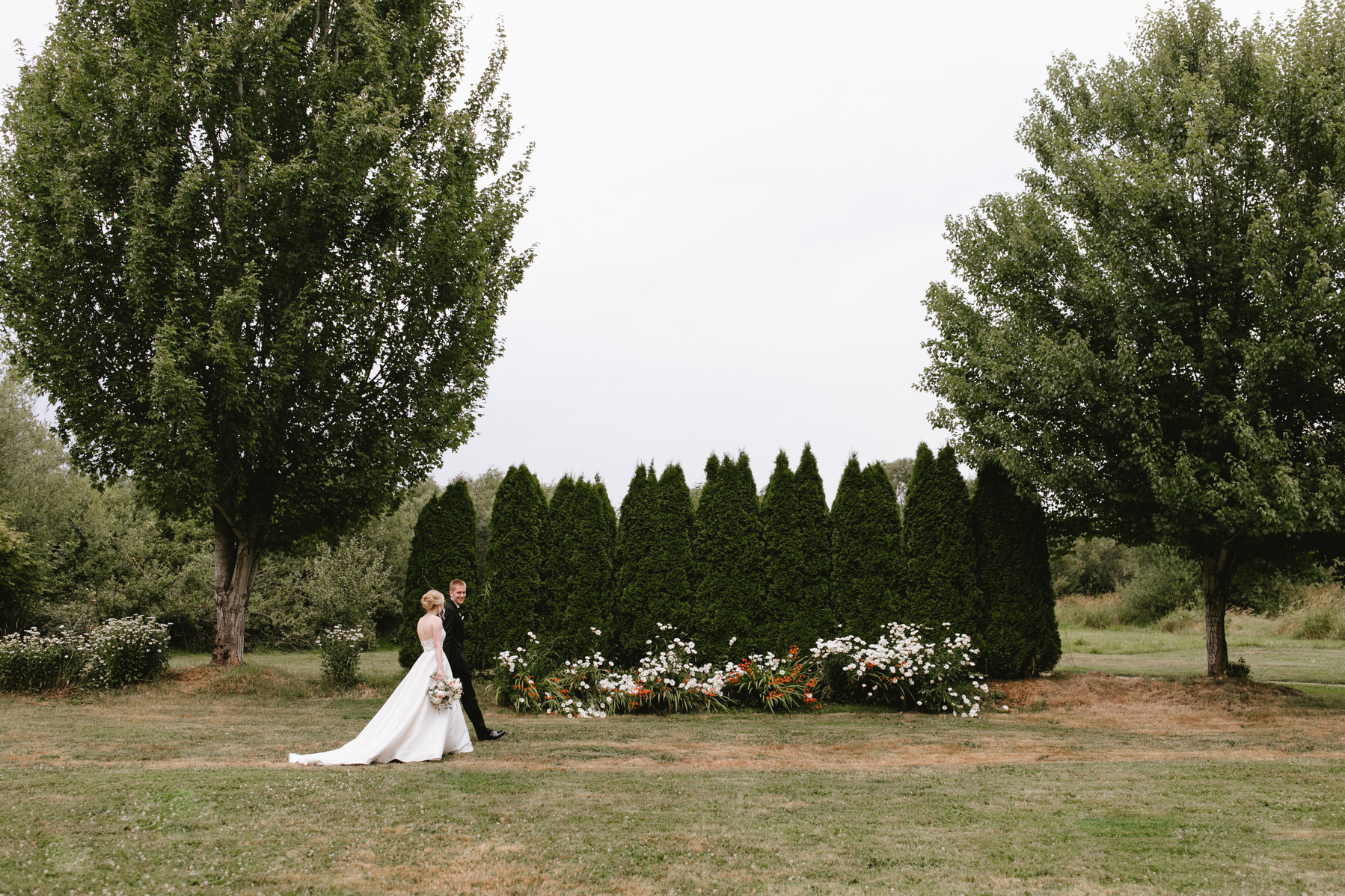 Washington bride and groom walking in her sweetheart wedding dress and his black tux toward a garden wedding of white roses