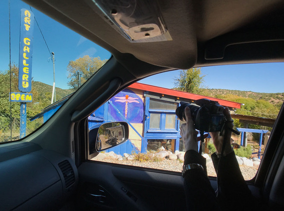 By Richard Barron, from The Winding Road. Captioned: Abby pokes her camera out the passenger side window to photograph an art gallery in Cundiyo, New Mexico.