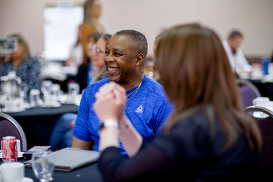 At a conference a man is smiling while listening to someone talk. 