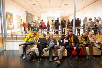 A group of people are sitting in the lobby during an art opening at the Madison Museum of Contemporary Art. 