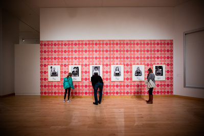 People are looking at art during an art opening at the Madison Museum of Contemporary Art. The wall is bright red and it's very beautiful. 